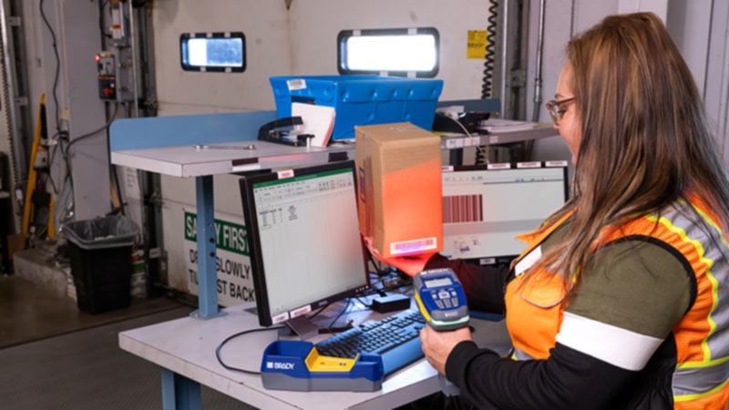 A warehouse worker scans an asset, and analyzes the scan using barcode software in an industrial setting.